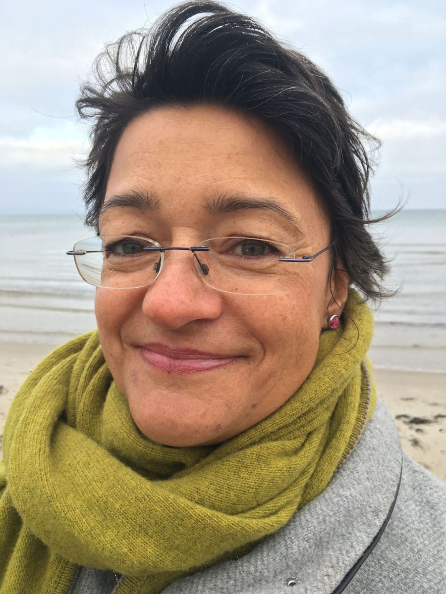 Antje Lode, lächelnd an der Ostsee, mit olivgrünem Schal
